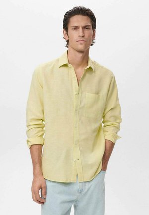 Camisa de lino amarilla clara con mangas largas, botones en el frente y un bolsillo en el pecho. Textura suave, mangas enrolladas y corte relajado.