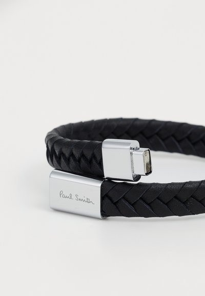 Musta punottu nahkakoru, jossa on hopeinen lukko ja kaiverrus "Paul Smith" lukossa. Liukas pinta ja tyylikäs muotoilu.