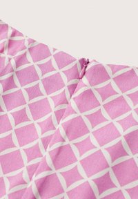 Vaaleanpunainen kangas, jossa on geometristä valkoista kuviota ristikkäisin linjoin. Lähikuvassa näkyy vetoketjun yksityiskohta ja sileä pinta.