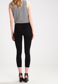 Černé skinny džíny s vysokým pasem, spárované s černobílým pruhovaným topem bez rukávů. Outfit je doplněn černými sandály na kotníky.