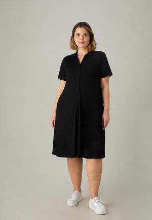 Sort kortærmet skjortekjole med knaplukning foran. Glat tekstur, knælang, båret med hvide sneakers. Minimalistisk design.