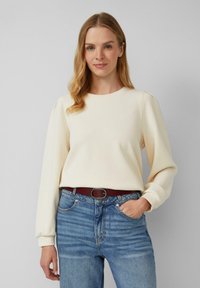 Crème sweatshirt met lange, puffy mouwen en een ronde halslijn, gecombineerd met blauwe jeans en een brown riem. Gladde textuur, casual ontwerp.
