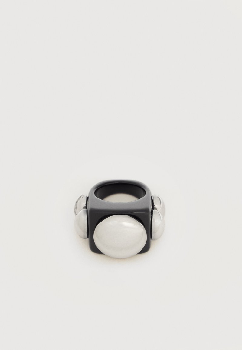 Μαύρο δαχτυλίδι σε σχήμα τετραγώνου με τέσσερις μεγάλες στρογγυλεμένες λευκές πέρλες στη μία πλευρά, πάνω σε λευκό φόντο.