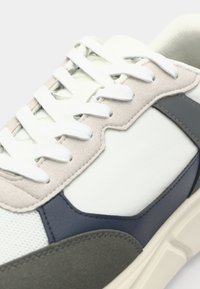 Sport shoes in white, gray, and navy blue. Features a mesh upper, suede accents, and a textured rubber sole with flat laces.