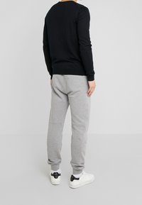 Svart stickad tröja, figursydd, med rund halsringning. Matchad med ljusgrå sweatpants, avsmalnande passform, med ribbade manschetter och sidofickor.