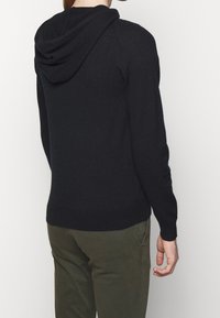 Schwarzer Kapuzenpullover aus weichem Stoff, mit lockerer Passform und gerippten Bündchen, ohne sichtbare Muster oder Logos.