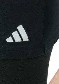 Zbliżenie czarnego materiału z białym logo Adidas, które zawiera trzy ukośne paski w pobliżu końca.