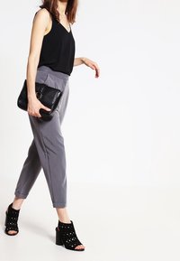 Svart ärmlös topp, grå skräddarsydda byxor, svarta perforerade öppna klacksandaler och en strukturerad svart handväska. Avslappnad outfit.