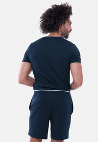 Marineblaues Kurzarmhemd mit glatter Textur und lockerem Schnitt, kombiniert mit passenden marineblauen Shorts mit Seitentaschen und elastischem Bund.