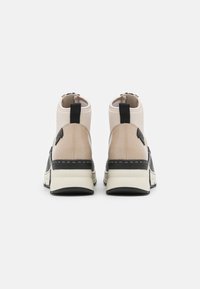 Bottines noires et beiges avec une texture lisse, un col rembourré, des poignées de tirage et une épaisse semelle blanche et noire. L'intérieur présente des coutures visibles.