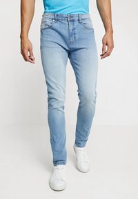 Jeans in denim azzurro chiaro con vestibilità slim, parte anteriore sbiadita, design a cinque tasche e cuciture a contrasto, abbinati a sneakers bianche.