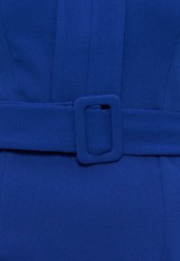 Κοντινό πλάνο μπλε υφασμάτινης ζώνης με τετράγωνη αγκράφα καλυμμένη από ύφασμα αντίστοιχου μπλε χρώματος σε ρούχο του ίδιου χρώματος.