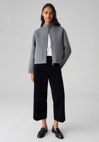 Grey fleece jacket with a high collar and front zip, paired with black corduroy wide-leg trousers and black loafers. Minimalist design.