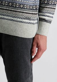 Gebreide sweater met geometrische patronen in marineblauw, grijs en crème. Beschikt over geribbelde manchetten en zoom. Gecombineerd met donkergrijze denimbroeken.