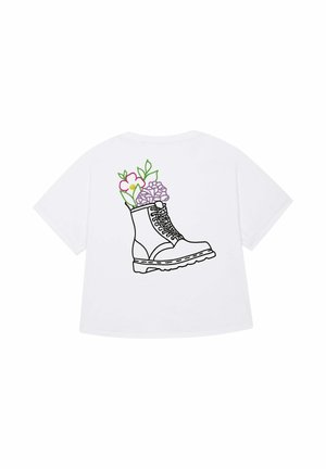 Witte t-shirt met een afbeelding van een zwarte laars gevuld met kleurrijke bloemen, waaronder een roze bloem en paarse bloemblaadjes.