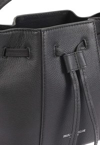 Zwarte leren emmer tas met een gestructureerde afwerking, gestrikte koordsluiting en een reliëf merklogo aan de onderkant.