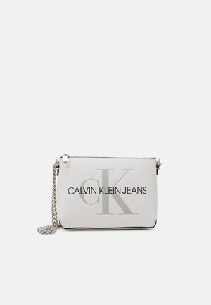 Biała prostokątna kopertówka Calvin Klein Jeans z srebrnym łańcuszkiem na ramię i zamkiem błyskawicznym na płaskim tle.