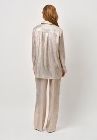 Glanzende, metalen gouden two-piece set bestaande uit een blouse met lange mouwen en een wijde broek. Soepele textuur met een ontspannen pasvorm.