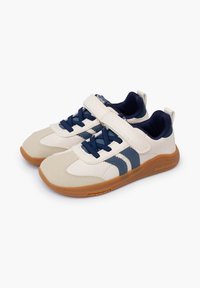 Sneaker con un design bianco e navy, dotate di dettagli in suede, una cinghia in velcro e una suola in gomma marrone con grip testurizzato.