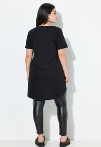 Black T-shirt dress with short sleeves and a rounded hem, paired with black shiny leggings and animal print slip-on shoes.