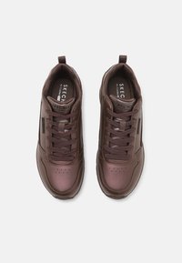 Brown athletic sneakers with a smooth, synthetic upper, round toe, lace-up design, and textured inner lining. Subtle perforations for breathability.
