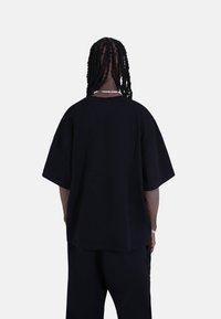 Black oversized t-shirt featuring short sleeves and a round neckline. Soft fabric with a smooth texture, worn with loose black pants.