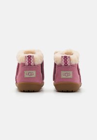 Bottines en suède rose avec doublure en fausse fourrure, tirette à motif et semelle texturée. Logo UGG sur la languette arrière. Design compact pour la chaleur.