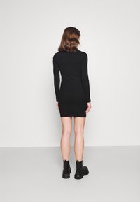 Robe noire à manches longues avec un design ajusté, longueur mi-genou et texture côtelée, associée à des bottines noires.