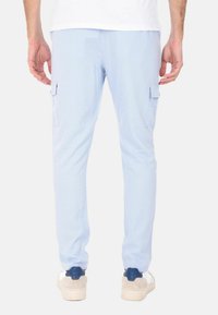 Pantaloni cargo azzurro chiaro con tasche laterali, vestibilità affusolata e texture morbida, abbinati a sneakers bianche e navy.