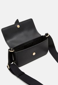 Bolso cruzado de piel negra con herrajes dorados, diseño minimalista y cierre de solapa. El interior cuenta con un forro de tela y una etiqueta con el logo.