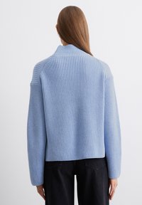 Hellblauer gestrickter Pullover mit gerippter Textur, überschnittenen Schultern und hohem Kragen. Verfügt über lange Ärmel und einen leicht verkürzten Schnitt.