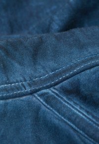 Denimstoff in tiefblau mit einer glatten Textur, der sichtbare Nähte aufweist. Nahaufnahme mit Fokus auf die Nahtdetails und die Stoffstruktur.