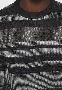 Stickad tröja med rund halsringning, svartvita horisontella ränder, texturerad tyg och en mysig, lätt känsla.