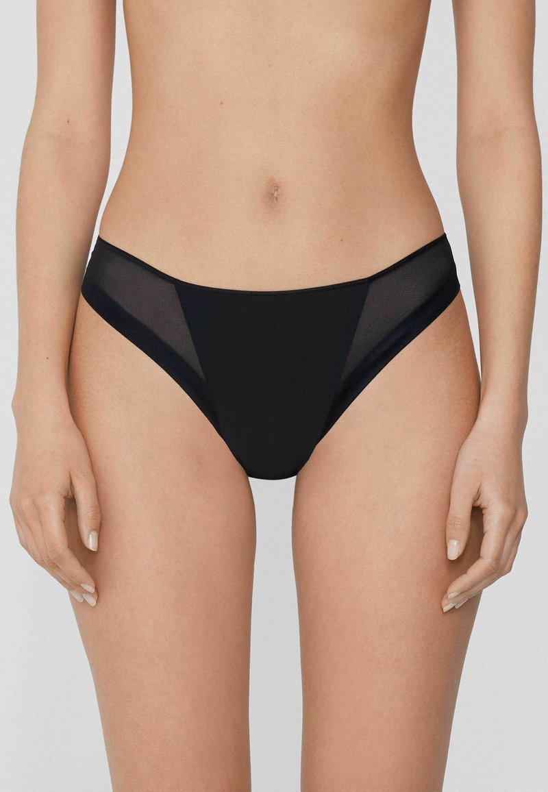Schwarze Bikiniunterhose mit einem nahtlosen Design und Netzakzenten an den Seiten, die eine glatte Textur und eine minimalistische Form betonen.
