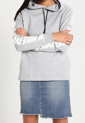 Hoodie gris avec une poche avant, cordons de serrage noirs et lettres blanches sur les manches. Associe à une jupe en denim bleu avec un ourlet effiloché.