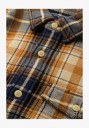Flannel shirt with a blue, orange, and cream plaid pattern. Features yellow buttons and a classic collar. Textured fabric with two chest pockets.