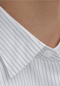 Chemise blanche à rayures verticales grises, avec un col boutonné et un tissu lisse légèrement texturé. Vue en gros plan du col.