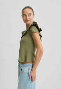 Oliven grøn kortærmet top med tekstureret flæsedetalje på skulderen. Stoffet er glat, og pasformen er afslappet og cropped.