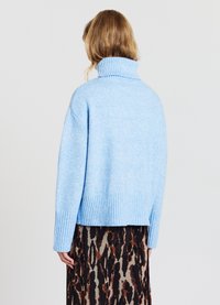 Hellblaue, gerippte Strickpullover mit hohem Kragen. Er hat eine lockere Passform und einen kurzen Saum, kombiniert mit einem gemusterten Rock.