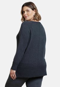 Mörkgrå stickad tröja med långa ärmar, rundad halsringning och en något längre bakre nederkant. Mjuk textur och minimal detaljer.