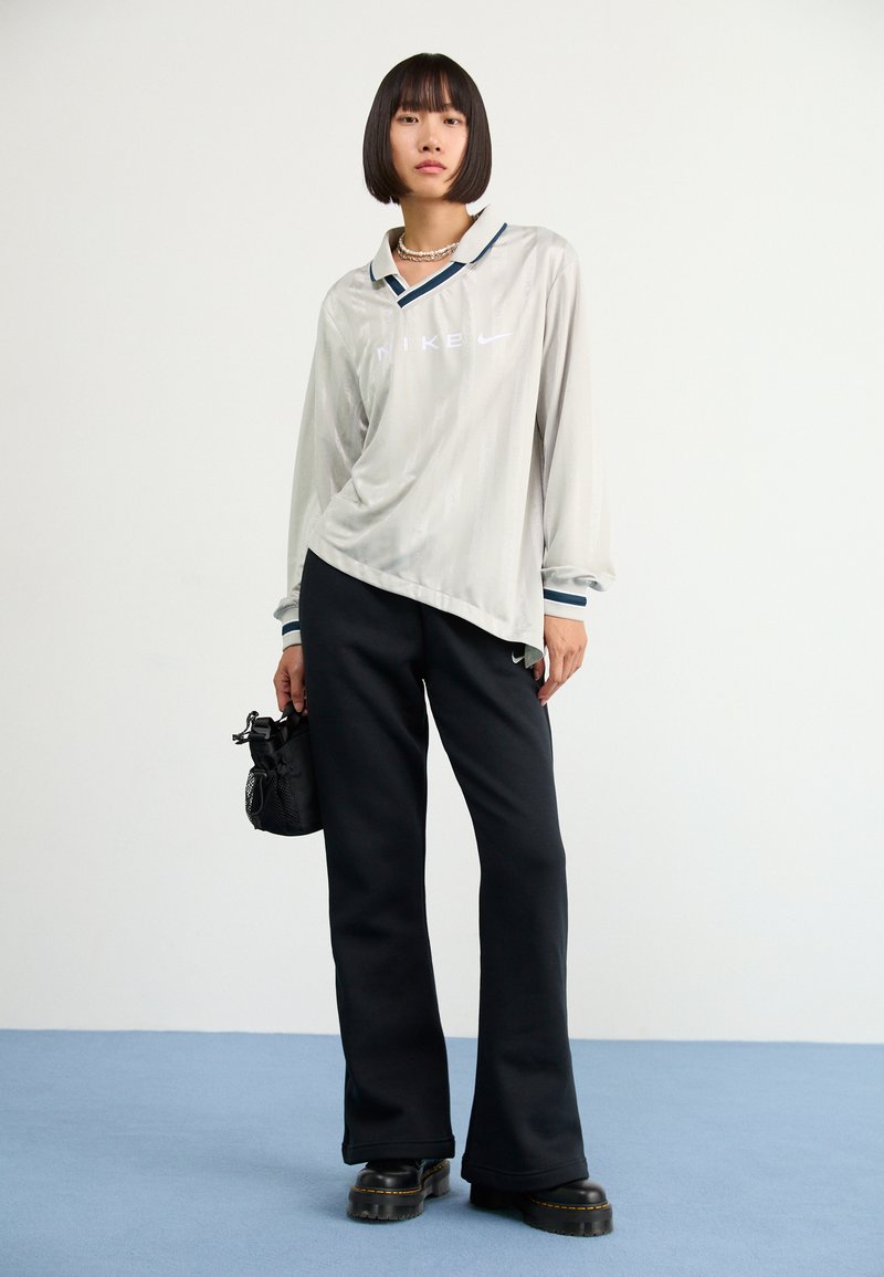 Chemise à manches longues Nike gris clair avec col, pantalon noir et bottes noires à plateforme. Présente des accents bleus et une légère brillance.