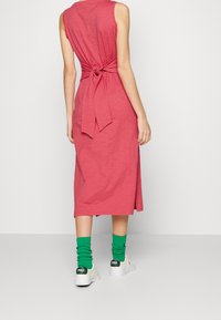 Ärmlös rosa midiklänning med knytning i midjan. Bärs med gröna scrunch-strumpor och vita sneakers. Slät tygkvalitet, avslappnad passform.