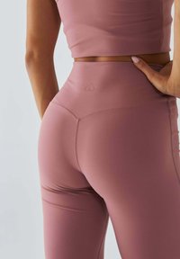 Legginsy z wysokim stanem, dopasowane, w delikatnym, stonowanym różowym kolorze. Posiadają subtelne logo w kształcie serca oraz gładki, elastyczny materiał z detalami przeszyć.