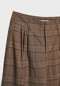 Jupe à carreaux marron avec des plis, une ceinture structurée et des lignes orange contrastantes sur tout le tissu à motif.