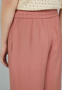 Lichtroze, loszittende broek met een elastische tailleband en zijzak. Gemaakt van zachte, gestructureerde stof, die een ontspannen silhouet laat zien.