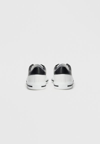White low-top sneakers with black heel accents, viewed from the back on a white background.