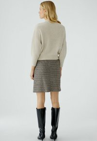 Beiger gerippter Pullover mit einem cropped Schnitt, kombiniert mit einem Rock im Hahnentritt-Muster und knielangen schwarzen Stiefeln, die ein strukturiertes Ensemble präsentieren.