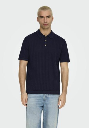 Marineblauwe geribbelde poloshirt met korte mouwen, drie knopen sluiting en contrasterende kraag. Draag het met lichtblauwe jeans.