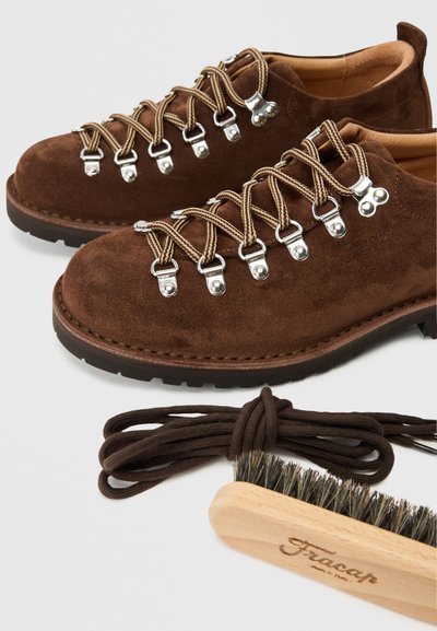 Brown suede hiking shoes with metal eyelets, brown flat laces, rugged sole, and a wooden brush. Includes extra laces.