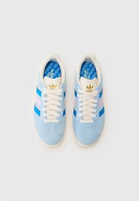Baskets en daim bleu clair avec des lacets crème, ornées de rayures bleues et roses et d'un logo doré sur la languette. Semelle intérieure décorative bleue.